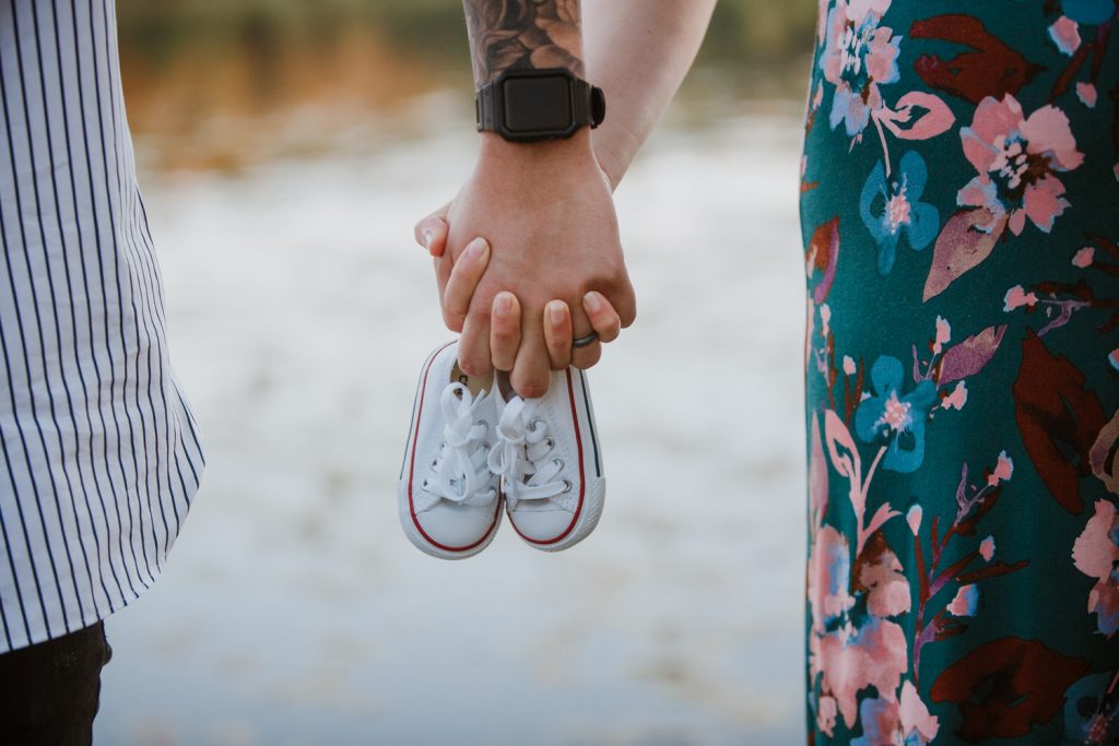 Married couple holding hands in a park while holding a baby shoe.