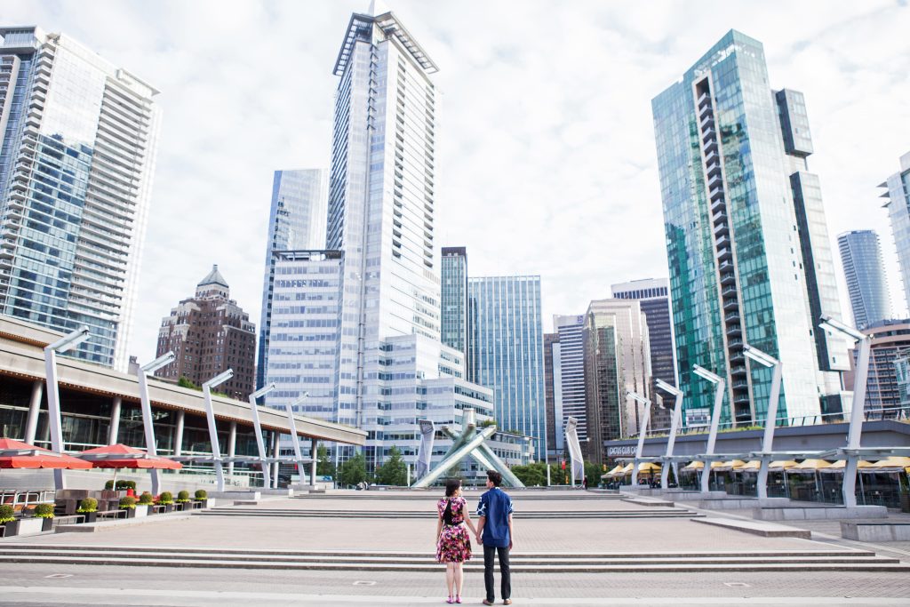 Urban engagement session of couple at Jack poole plaza while holding hands with the Vancouver financial district in the background