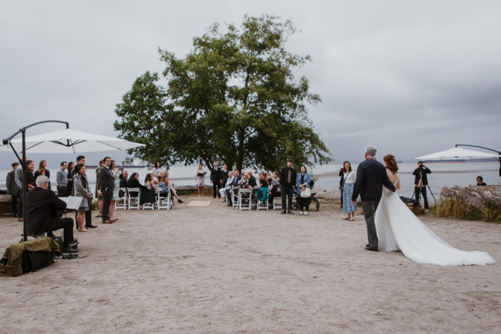 Wide angle of guests seeing the bride walk down the aisle in Spanish Banks