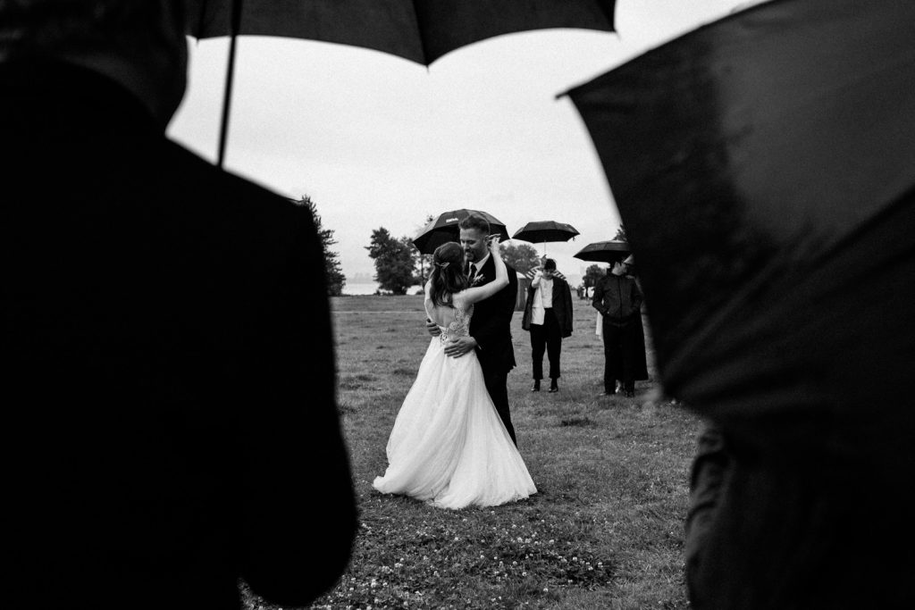 Black and white candid romantic photo of bride and grooms first dance under the rain in spanish banks