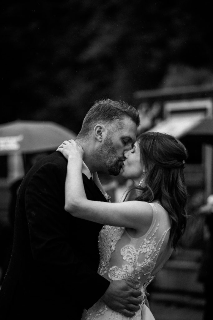 Black and white photo of the bride and groom kissing under the rain during their first dance in spanish banks